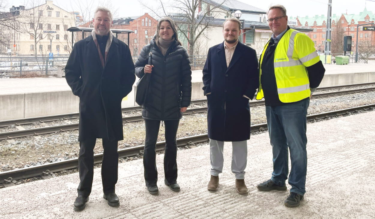 Fyra personer står på tågperrongen på Gävle central. Tre av dem bär mörka kläder och en person står med varselväst.