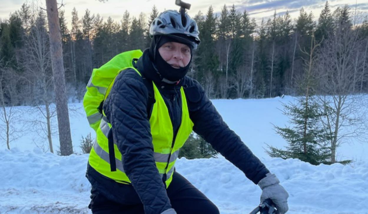 Peter Rens på sin cykel i vinterlandskap. Han har på sig en reflexväst och på hjälmen ser man en pannlampa. 