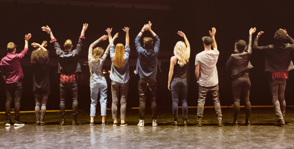 Back view of group of young performers on the stage standing in the line. Dark tones.