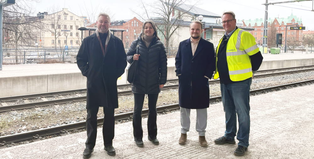 Fyra personer står på tågperrongen på Gävle central. Tre av dem bär mörka kläder och en person står med varselväst.