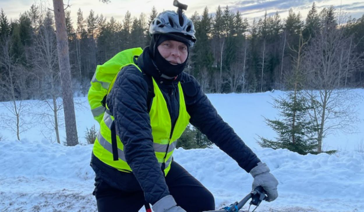 Peter Rens på sin cykel i vinterlandskap. Han har på sig en reflexväst och på hjälmen ser man en pannlampa. 