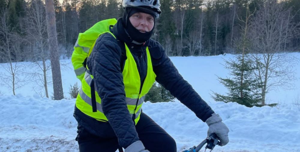 Peter Rens på sin cykel i vinterlandskap. Han har på sig en reflexväst och på hjälmen ser man en pannlampa. 